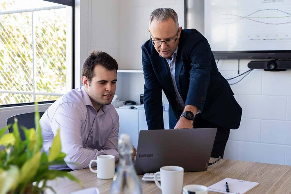 Andrew Foote, Director at Hunter Withers, collaborating with a team member while reviewing a laptop screen at the Pukekohe office.