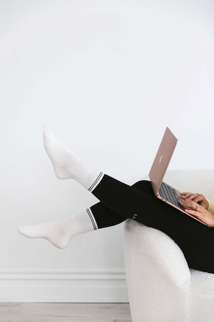 Close-up of Emma Bracken’s feet in soft white crew socks, playfully kicked up as she types on her laptop, capturing a relaxed and focused work-from-home vibe.