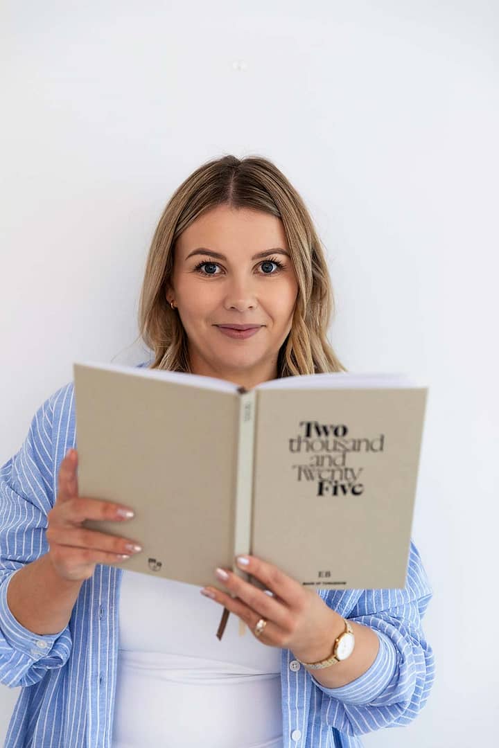 Emma Bracken, a financial advisor, smiling warmly at the camera while holding up a 2025 planning diary in a bright, professional setting.