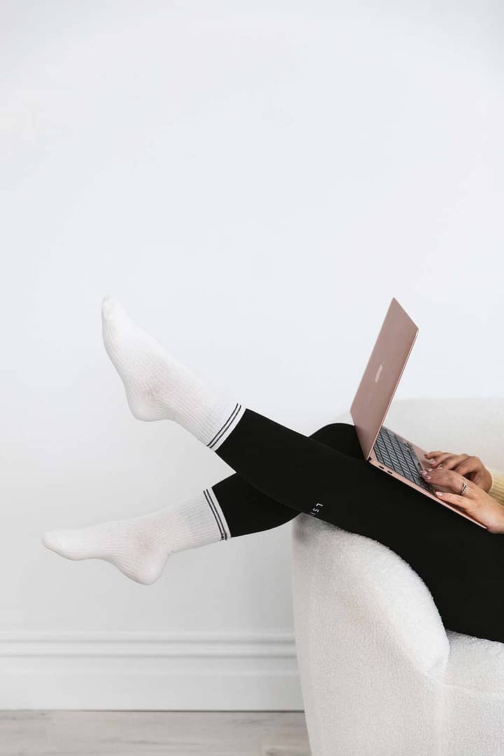 Close-up of Emma Bracken’s feet in soft white crew socks, playfully kicked up as she types on her laptop, capturing a relaxed and focused work-from-home vibe.